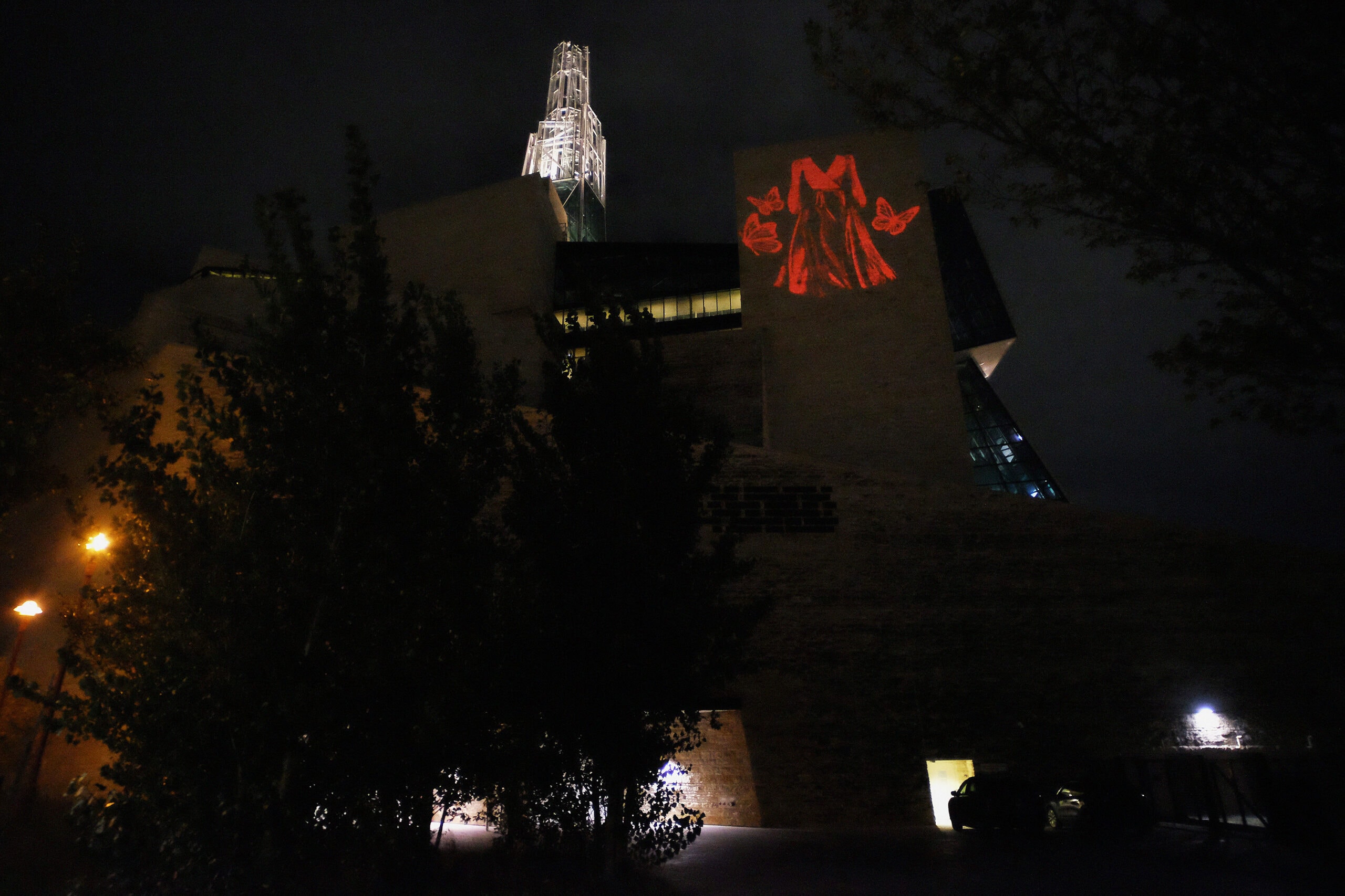 A projection of red light in the shape of an empty red dress accompanied by butterflies on the Canadian Museum of Human Rights building, honouring the ongoing MMIWG2S+ crisis.