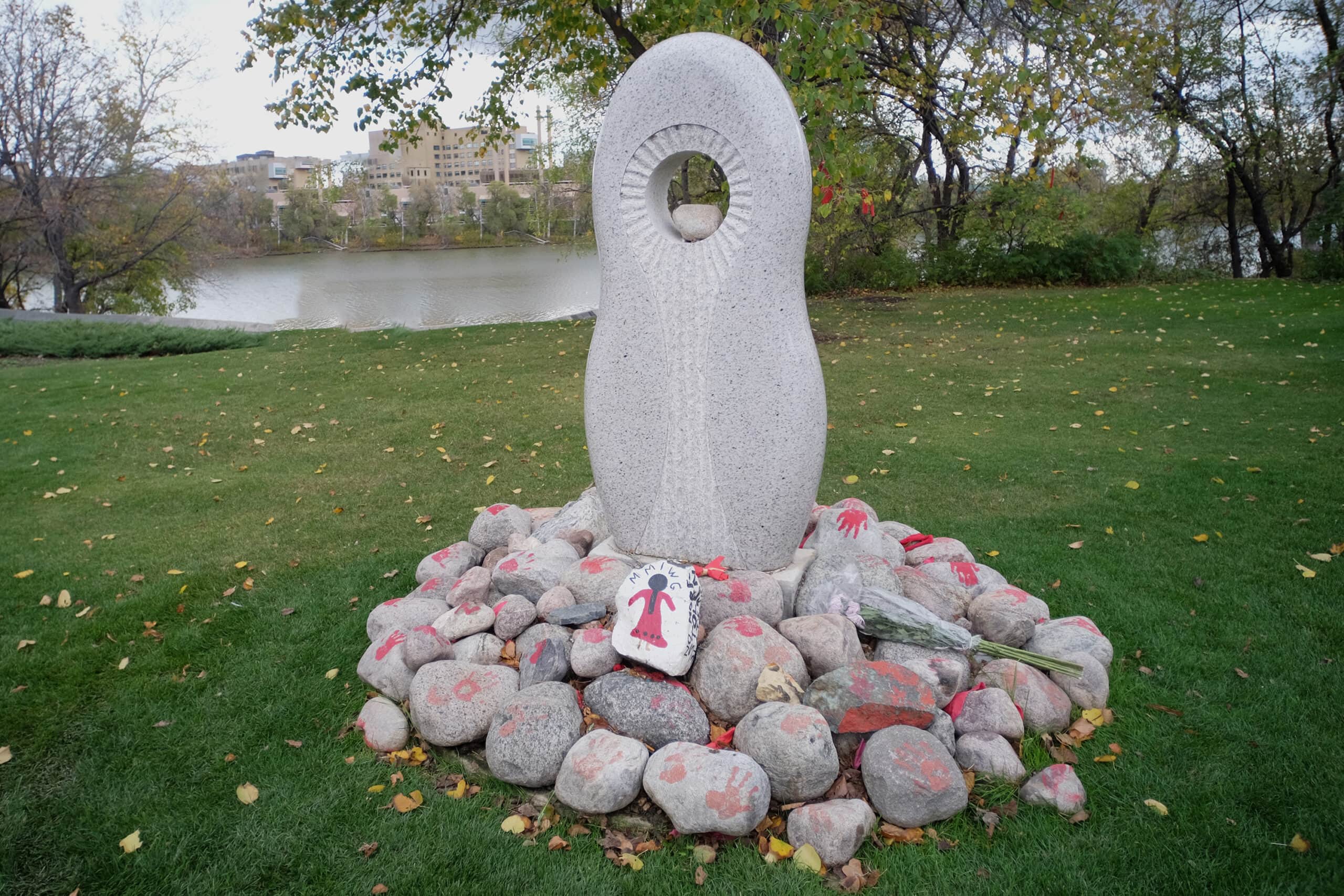 Un monument se dresse sur le bord de la rivière Rouge au Manitoba. Ce monument est entouré de roches avec des empreintes de mains rouges peintes, des fleurs, d'autres messages et de petits objets dédiés aux membres de la famille touchés par la crise des femmes, des filles et des personnes autochtones disparues ou assassinées.